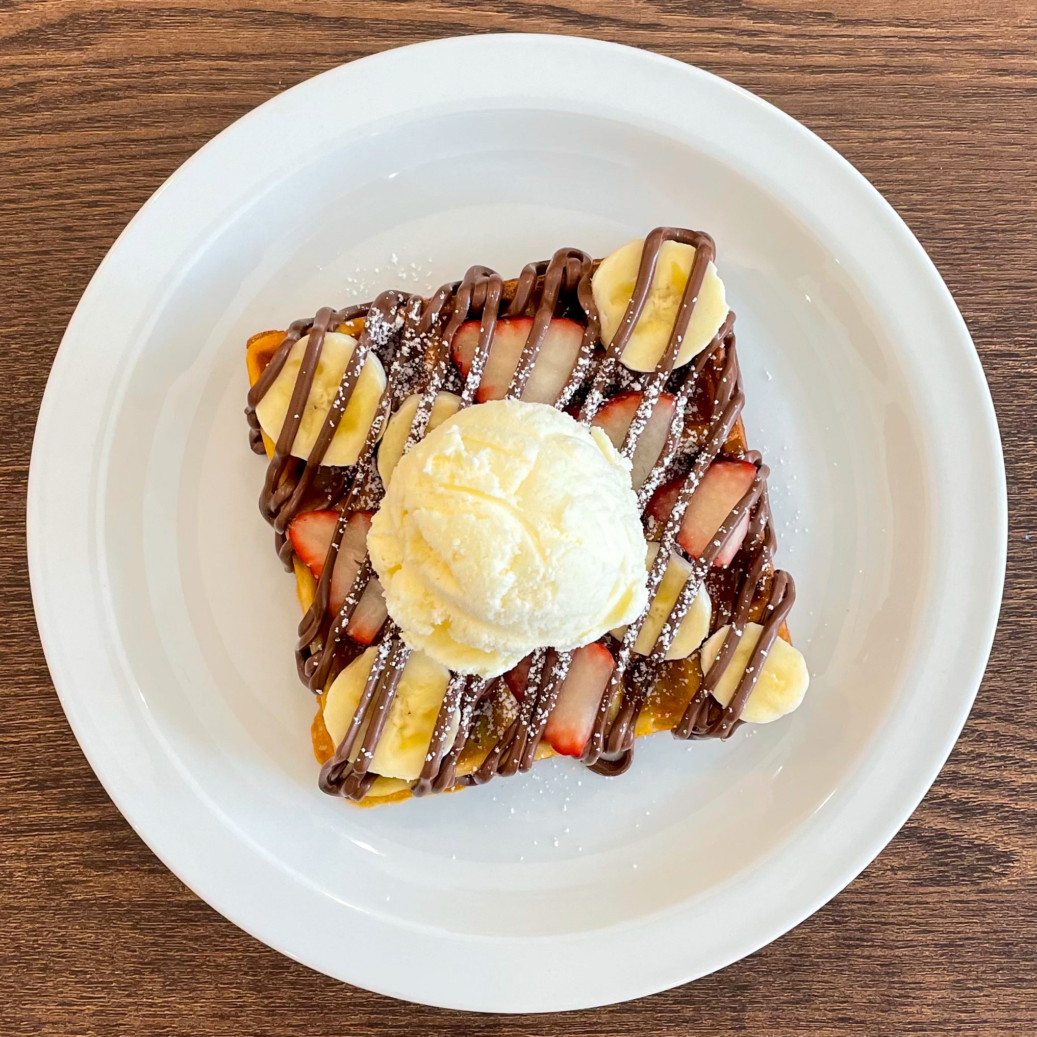 Nana's fluffy buttermilk waffle with fresh strawberries & bananas. Topped with Nutella & icing sugar!